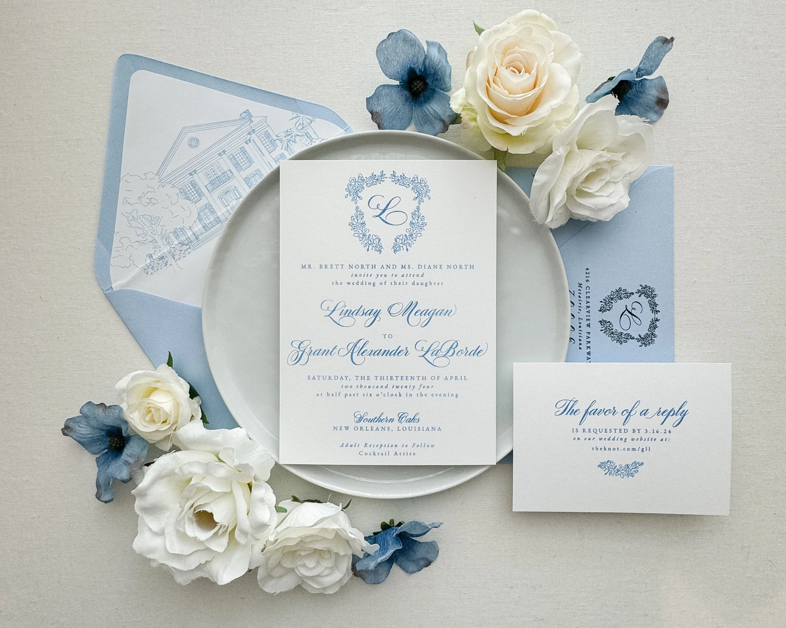 Elegant wedding invitation set styled with a main invitation card, RSVP card, and envelope, featuring a pale blue and white color scheme. The layout includes floral accents with white and blue flowers.