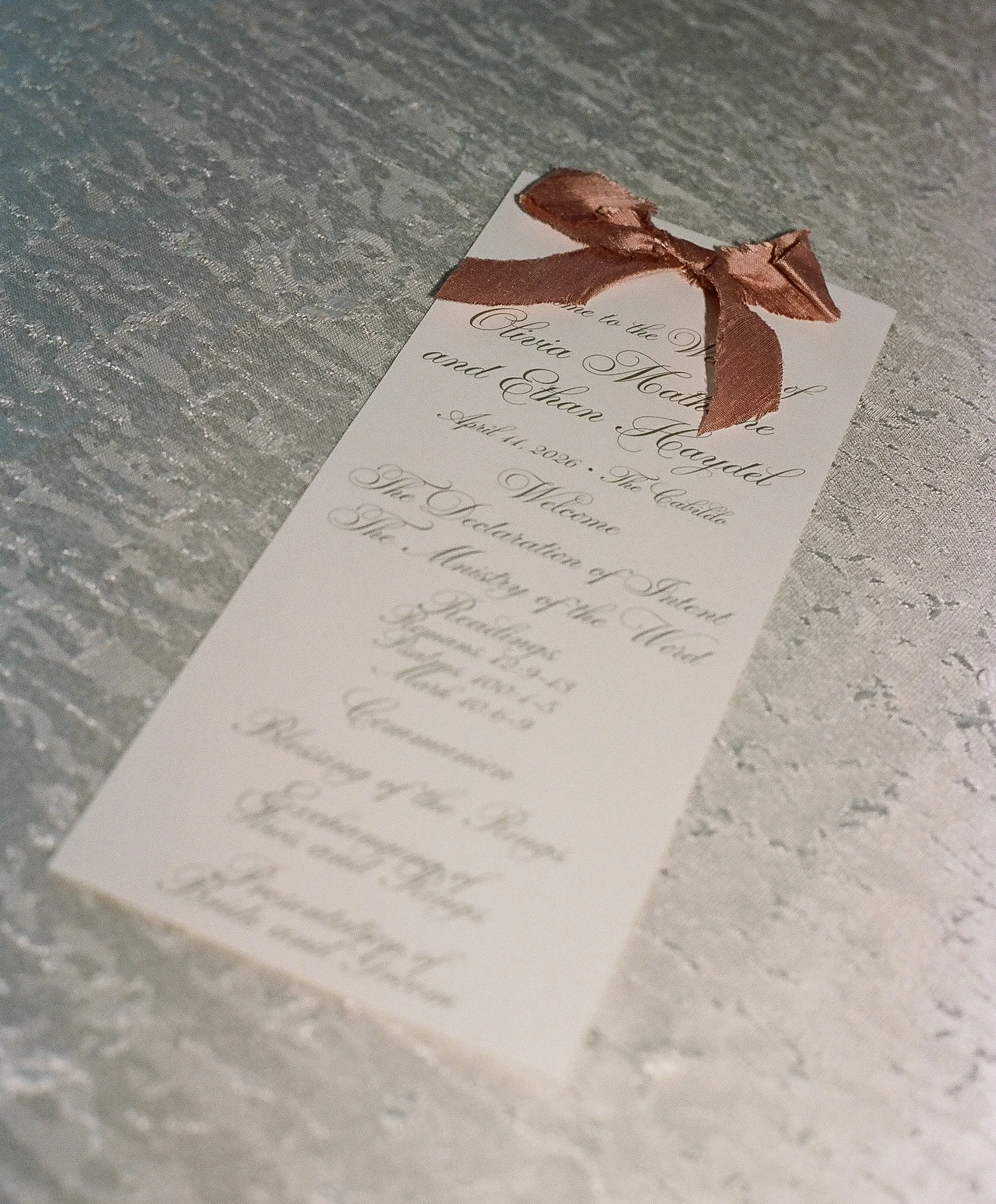 Ivory wedding ceremony program tied with a dusty rose silk ribbon bow
