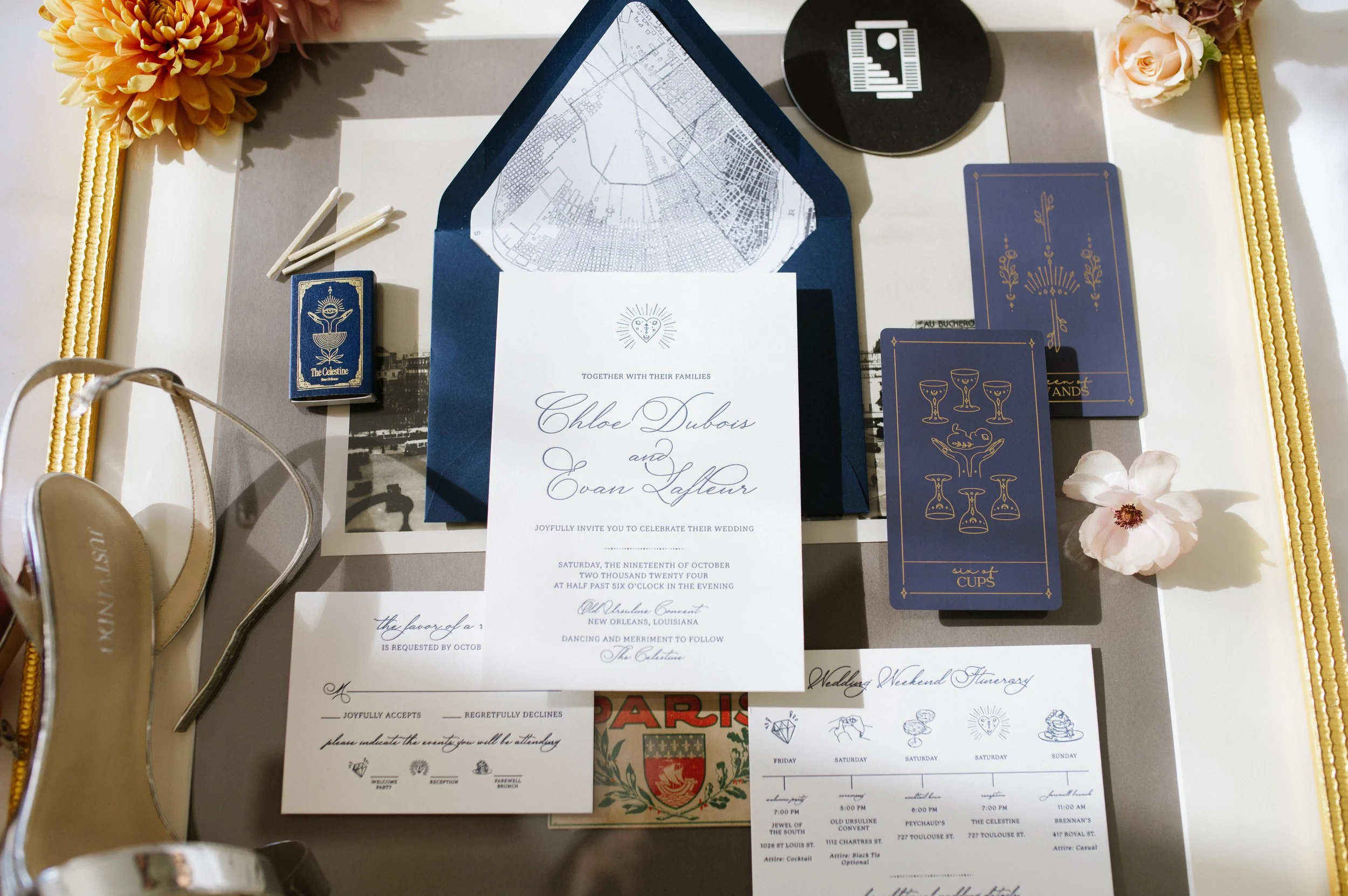Wedding invitation set with blue envelope, floral decorations, golden shoes, tarot-style cards, and a schedule of events.