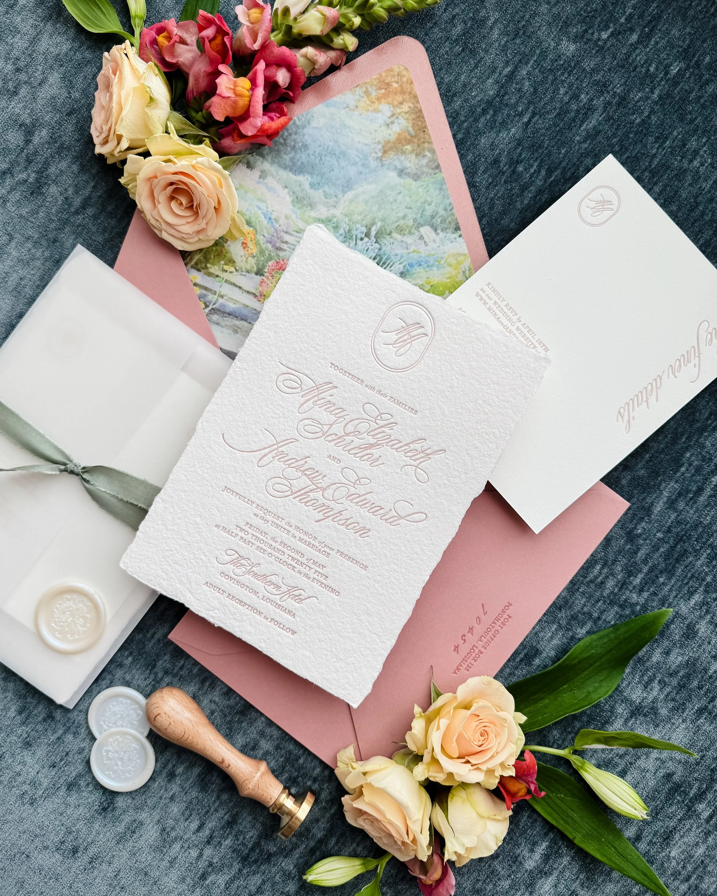 Elegant wedding invitation suite with blush pink and watercolor garden accents, decorated with fresh cream and peach roses, and sealed with wax, on a denim surface.