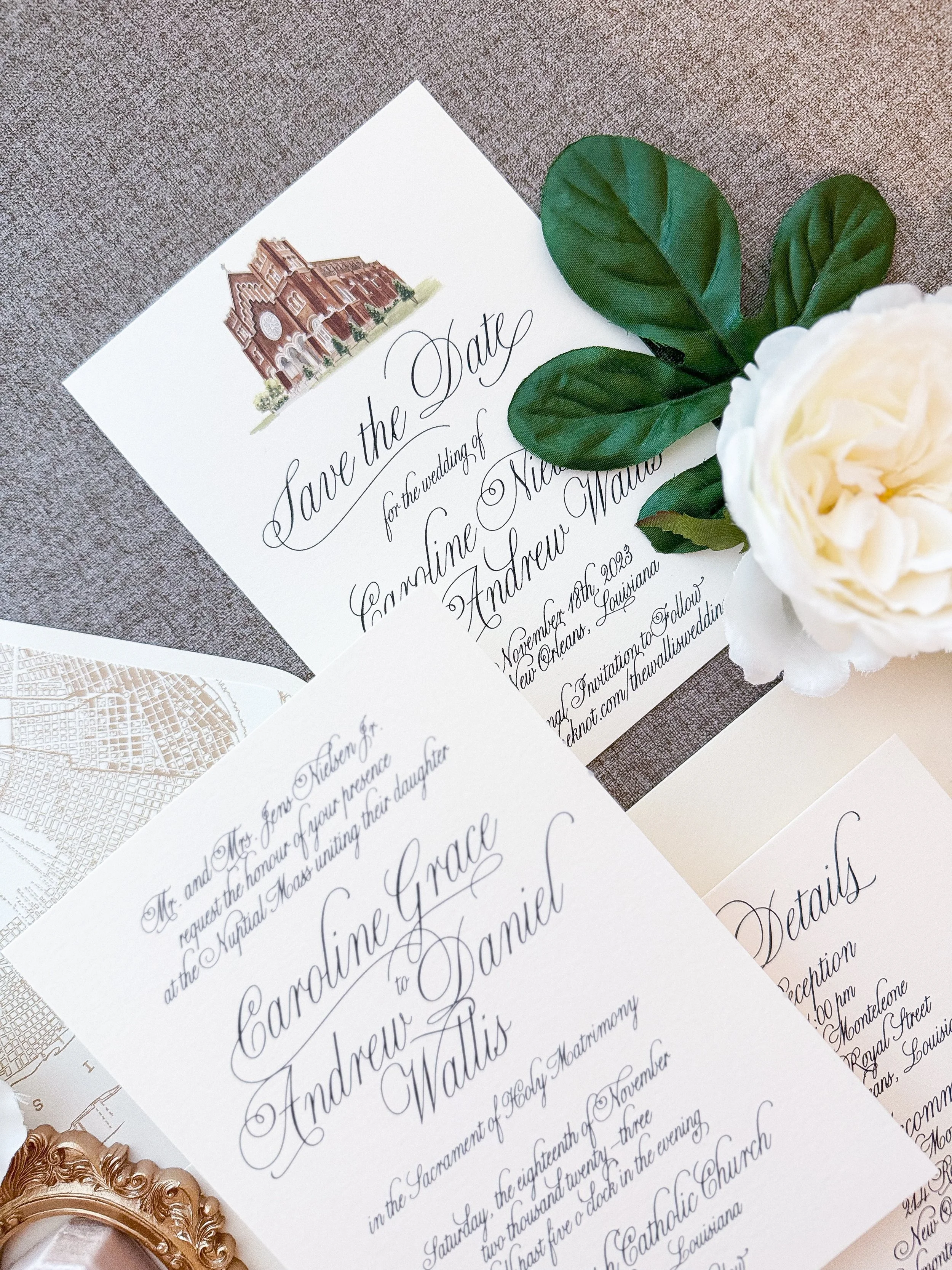 Wedding invitation cards with elegant calligraphy, a white rose, and green leaves, placed on a textured gray surface.