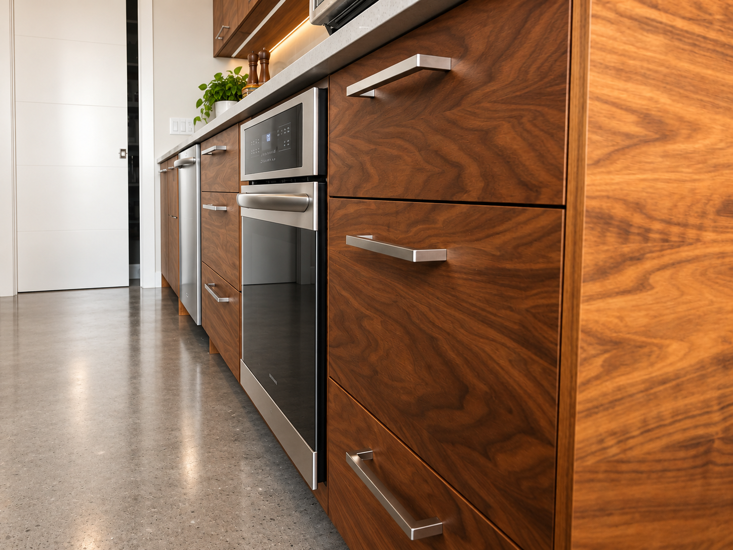 Close-up of custom walnut kitchen cabinetry with deep drawers, integrated appliances and natural wood grain.