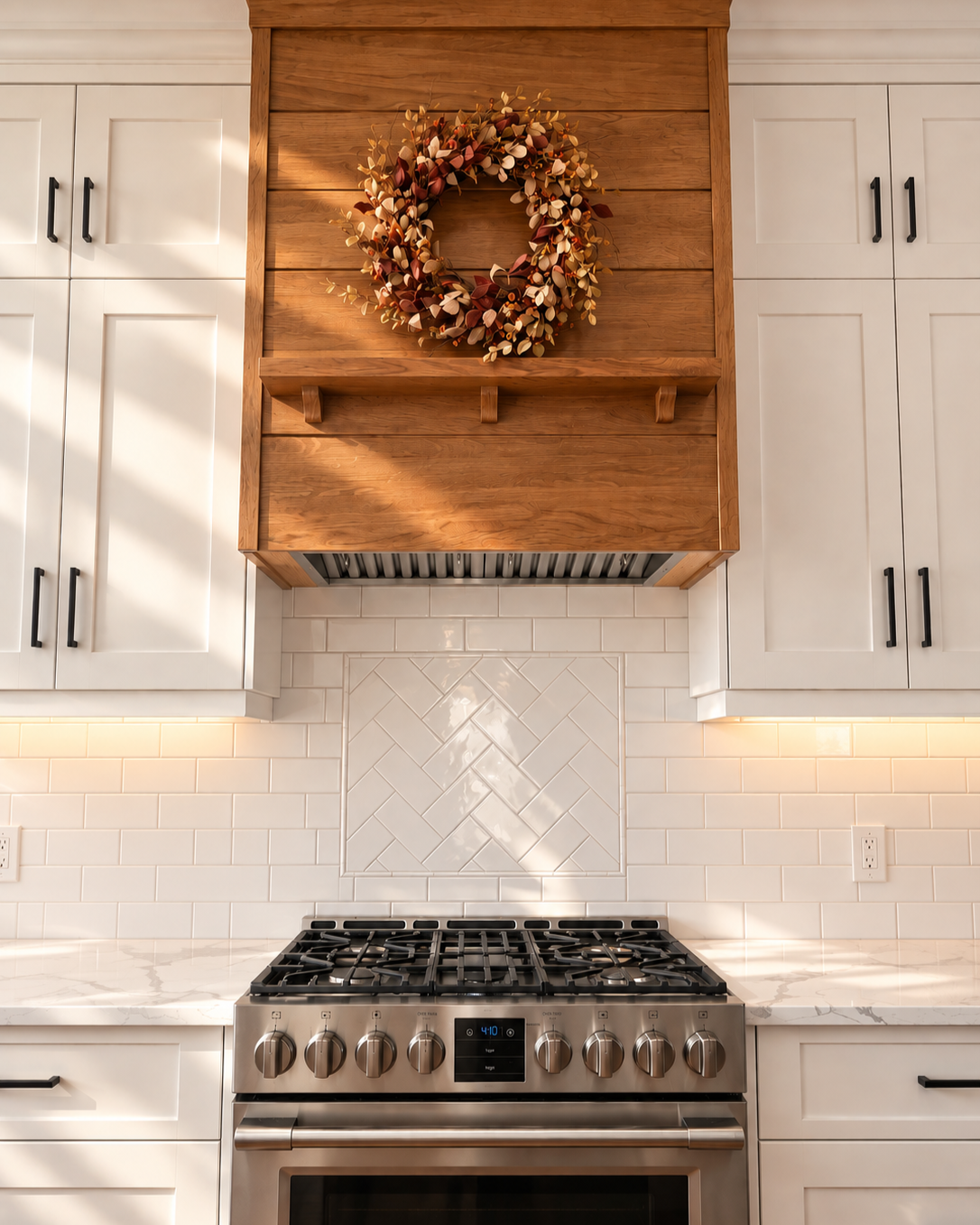 Handcrafted white oak range hood with white Shaker cabinetry and white tile backsplash.