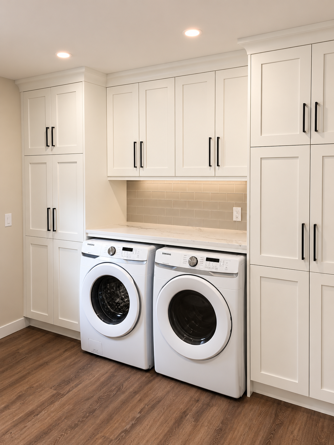 Custom white laundry room cabinetry with built-in storage, stone countertops and space for front-loading appliances.
