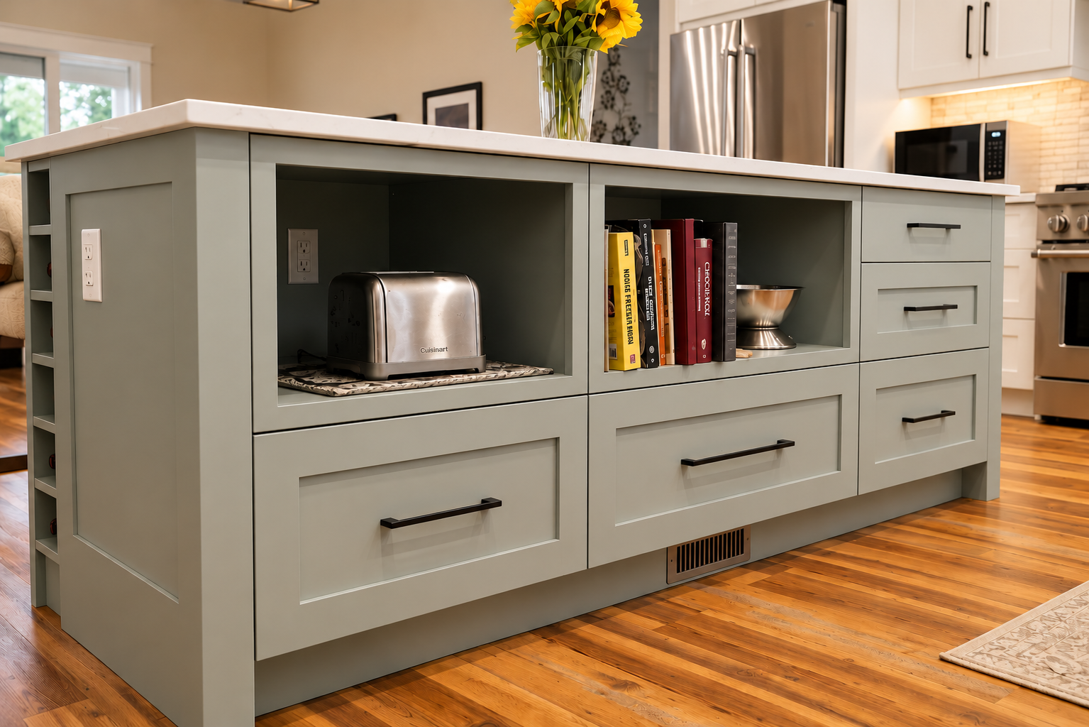 Custom sage green kitchen island with open shelving for cookbooks and appliances, built-in drawers, black hardware and a white countertop.