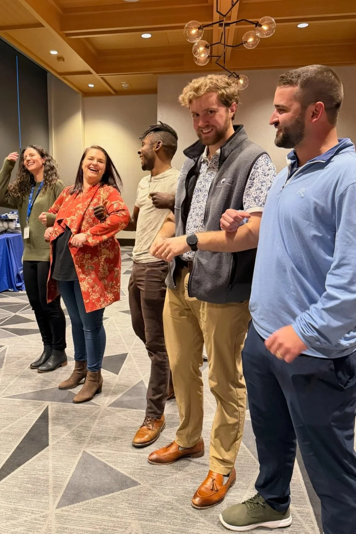 Group of six diverse people standing in a line and laughing at an indoor event.