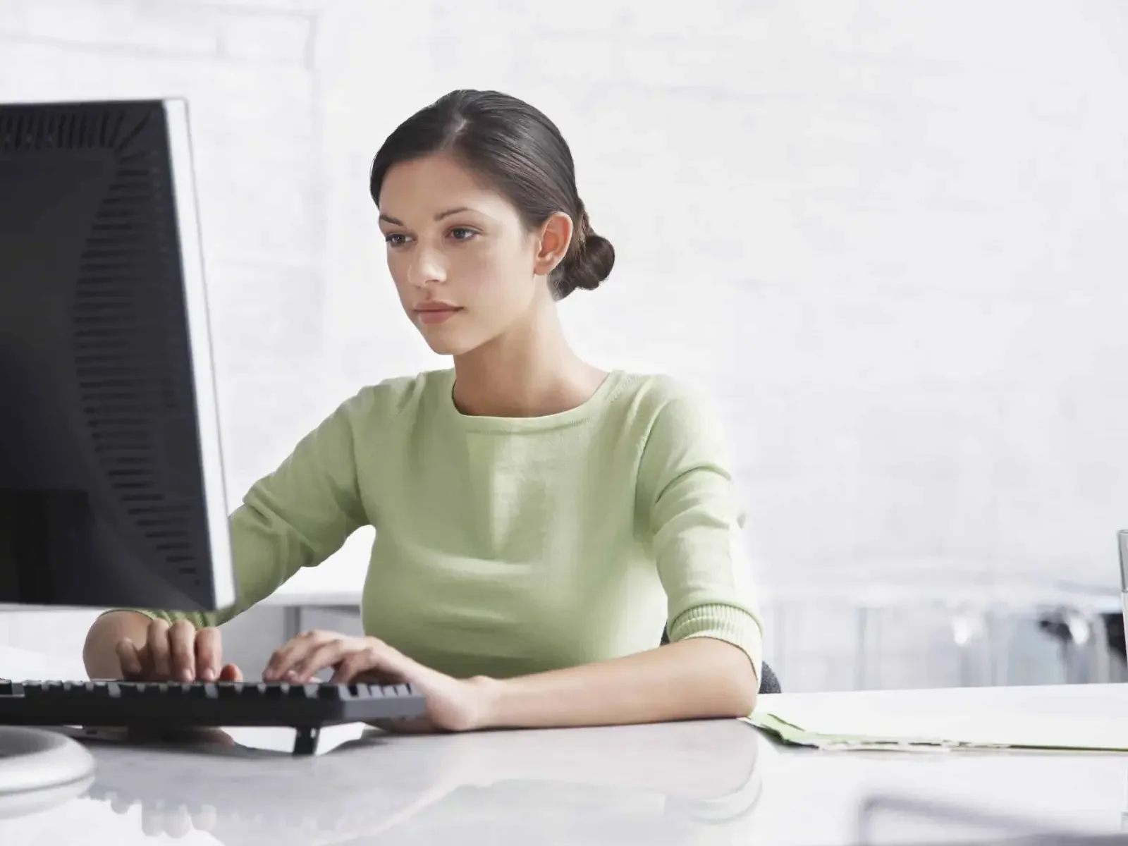 A woman with dark hair styled in a bun working at a computer in a bright office.