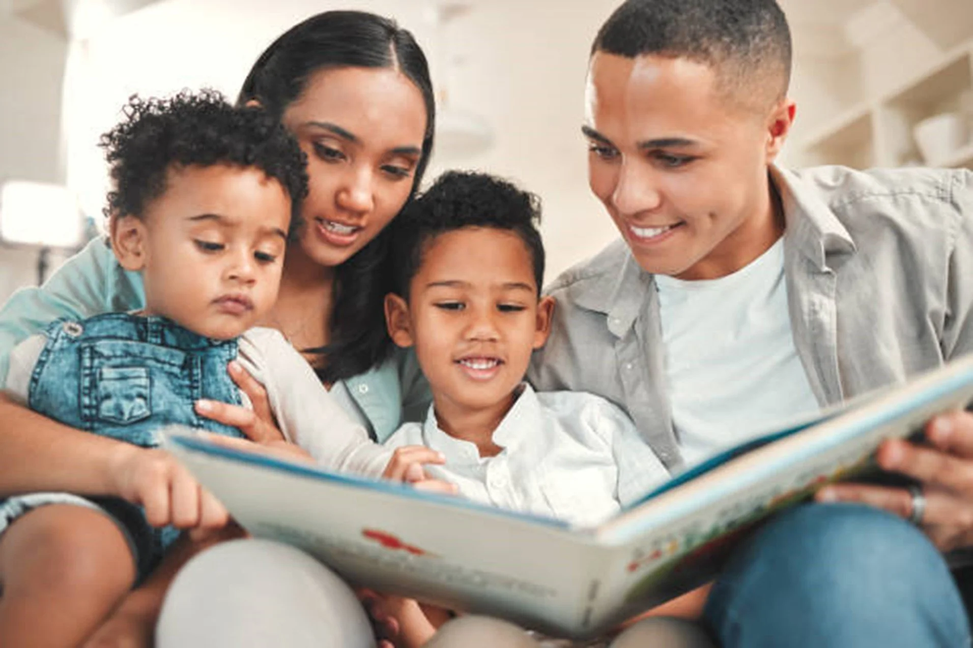 Family of five reading a book together on a couch in a cozy home.