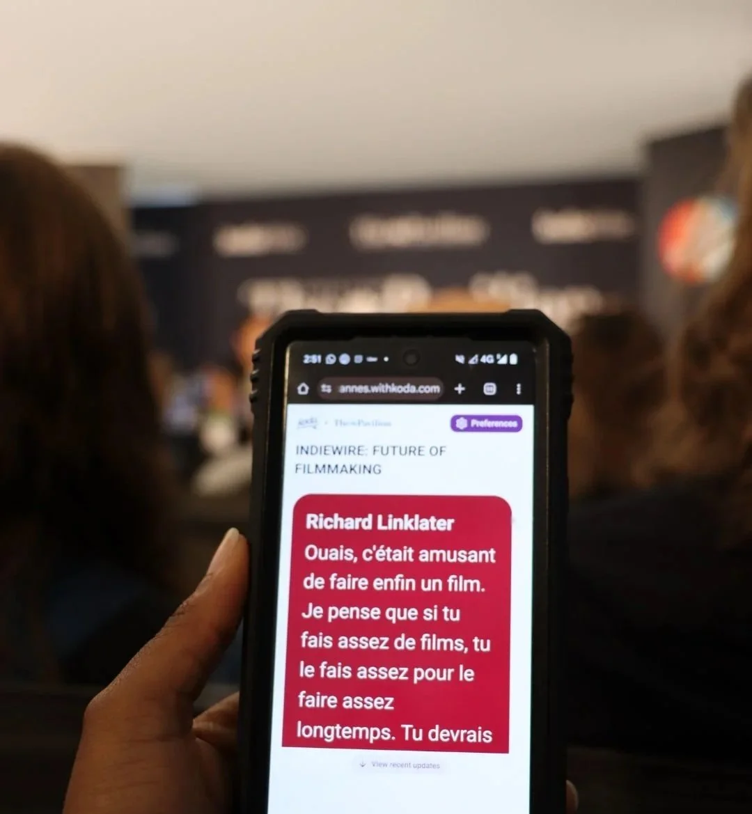 A panel session at the Cannes Film Festival, with a smartphone screen showing Koda live captions translating filmmaker Richard Linklater’s remarks into French in real time.