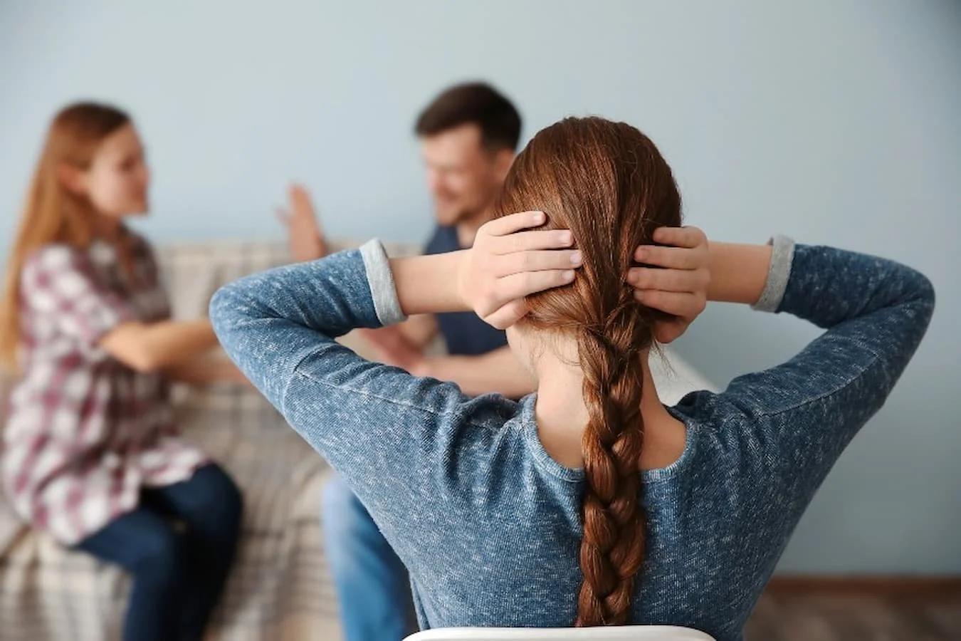 Young child covering ears with hands while parents appear to be arguing
