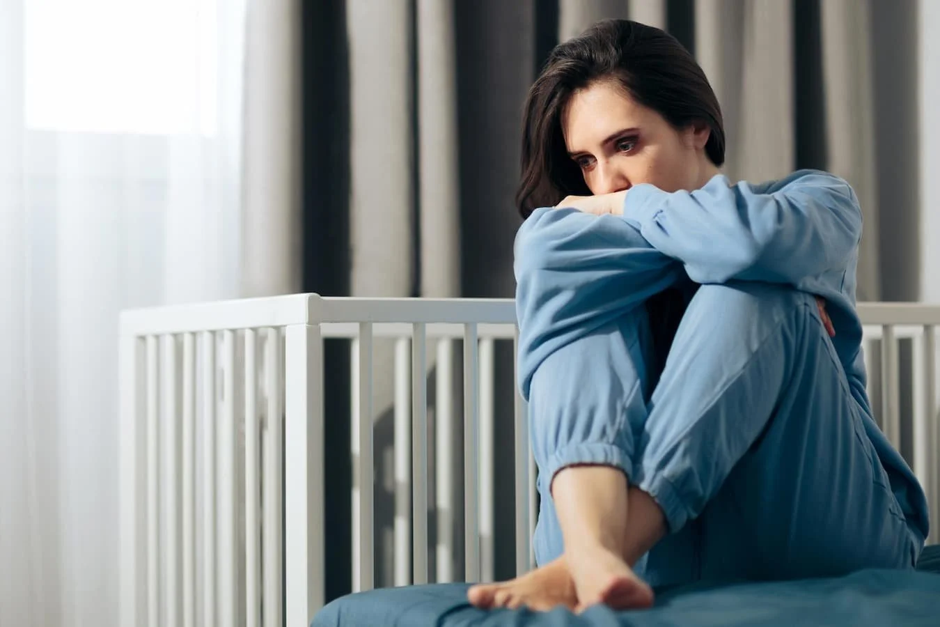 Woman sitting by an empty crib looking sad