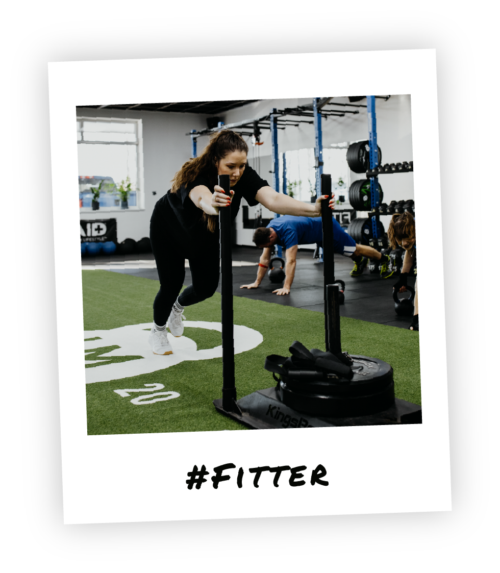 Functional Training bei HM Fitness – Frau beim Sled Push im intensiven Ganzkörpertraining im Stil eines Polaroid-Fotos und dem Hashtag "Fitter" drauf geschrieben.