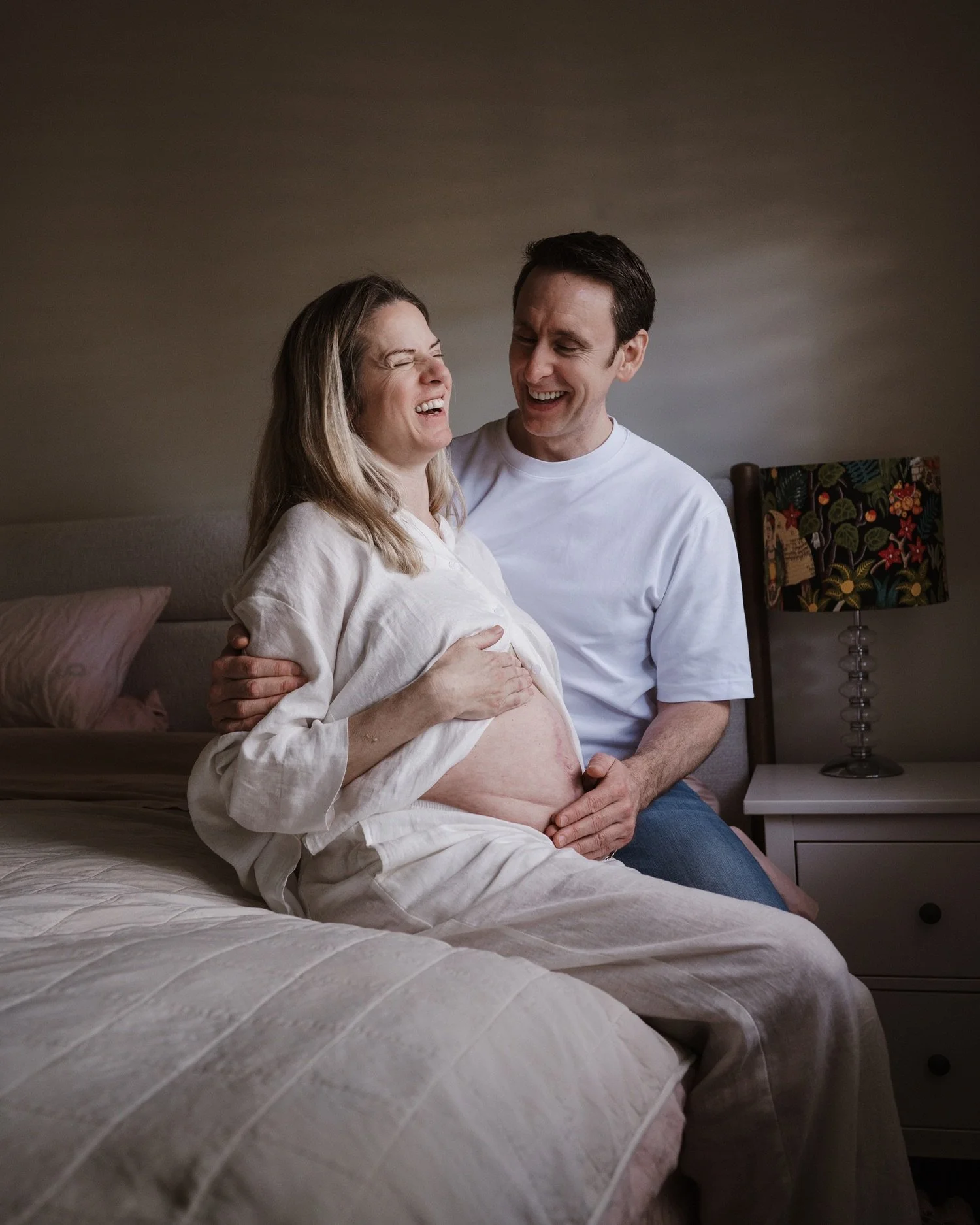 A pregnant woman and a man smiling and laughing together in a bedroom.