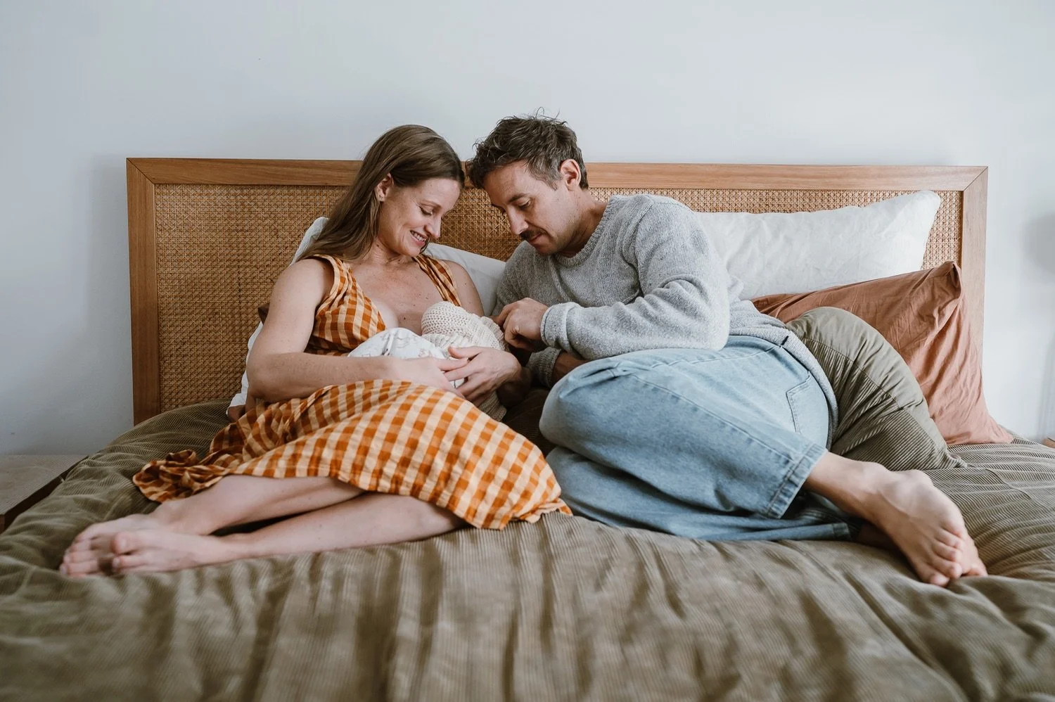 A couple with a newborn baby in bed, smiling and looking at the baby.