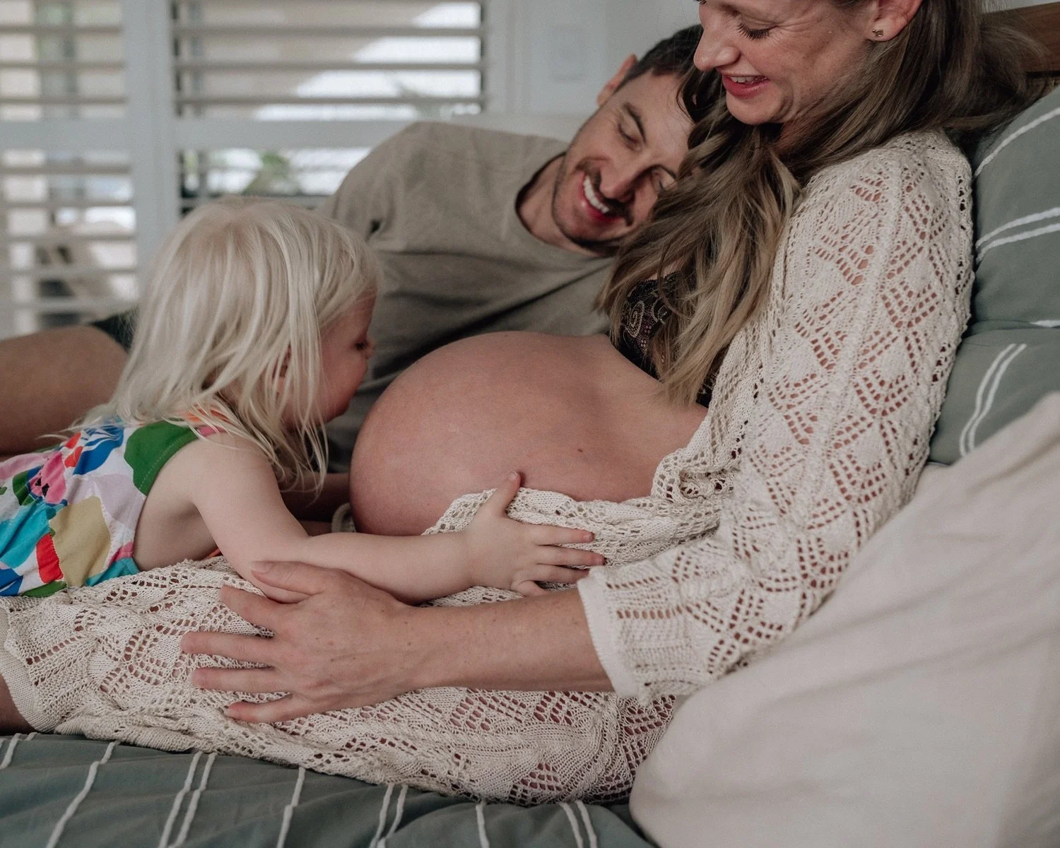 Pregnant woman with her partner and daughter in a cozy bedroom.