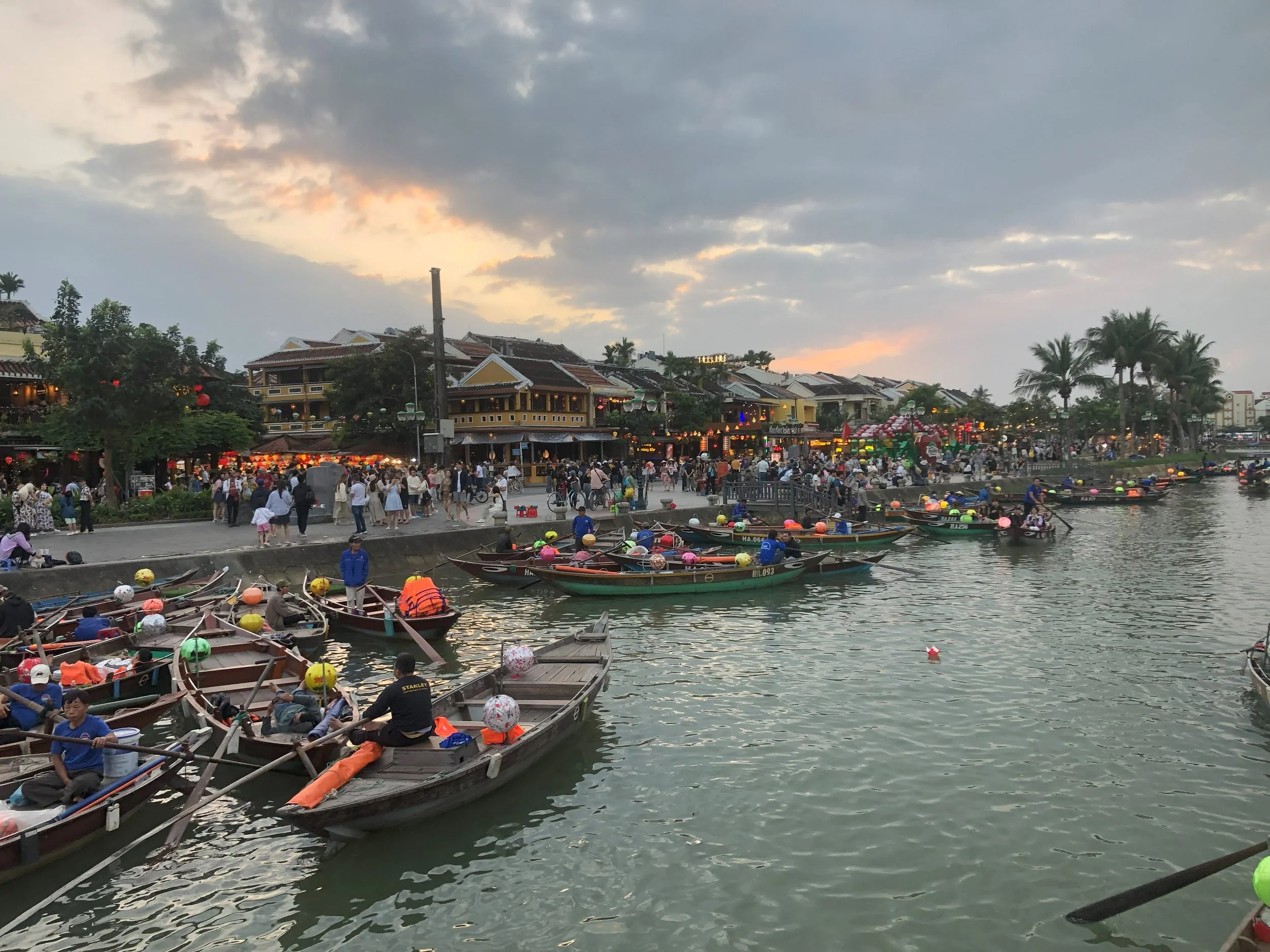 Scenic riverfront at dusk with traditional boats and a lively crowd, symbolizing G Group’s vibrant community and collaborative spirit in business consulting.
