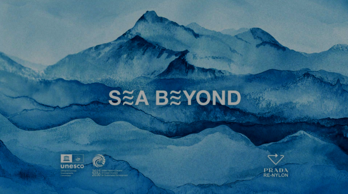 Un'immagine con sfondo di montagne blu e il testo "SEA BEYOND" al centro. In basso a sinistra i loghi di UNESCO e altri enti, e in basso a destra il logo di Prada Re-Nylon.
