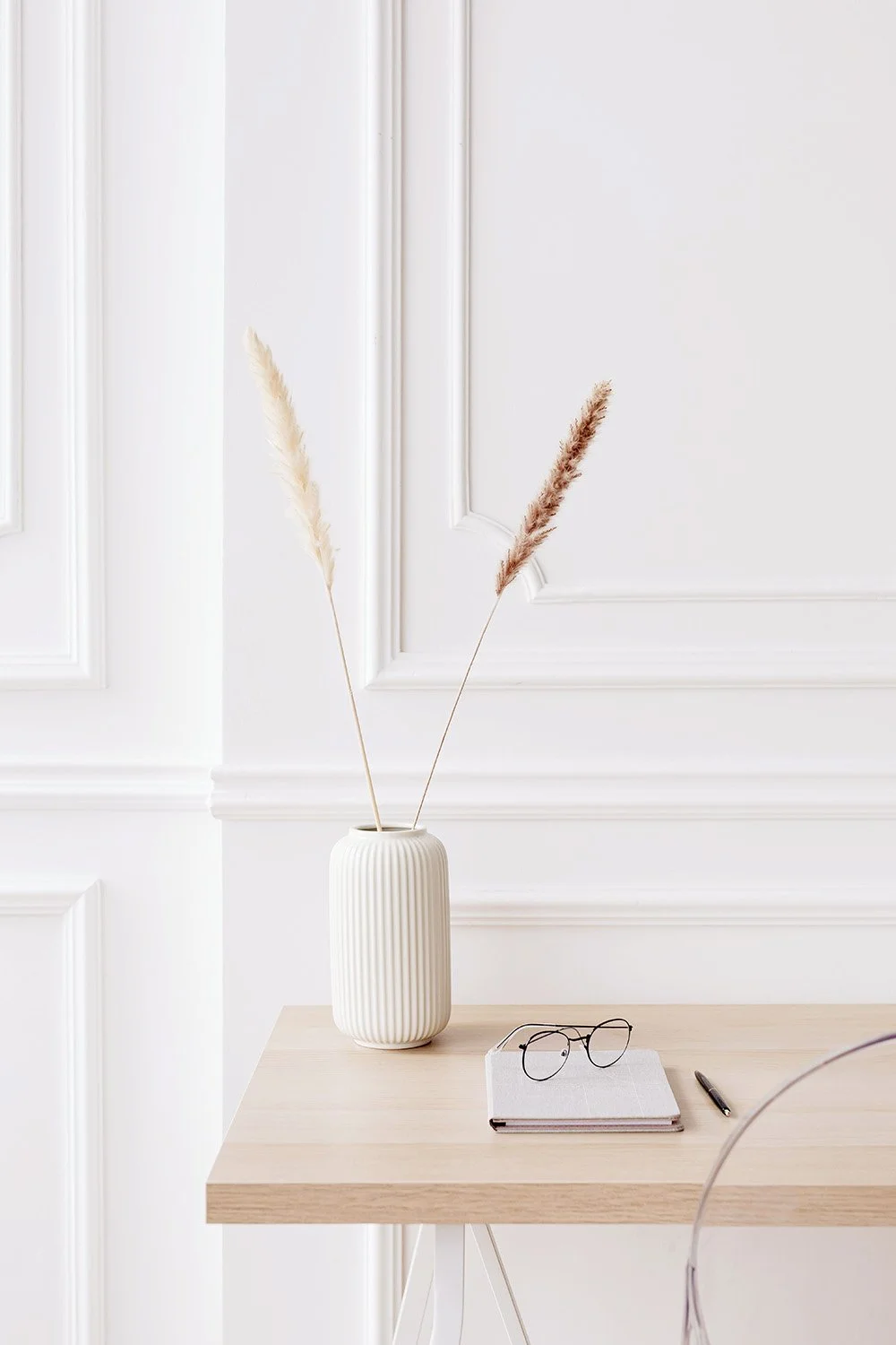 Light and airy image of a desk with a vase, glasses and notebook