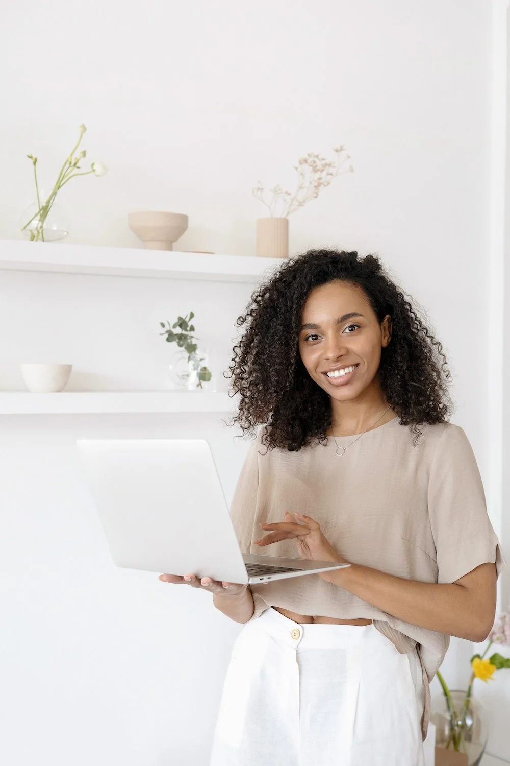 Photoshoot example: woman standing with laptop and minimal white shelves behind