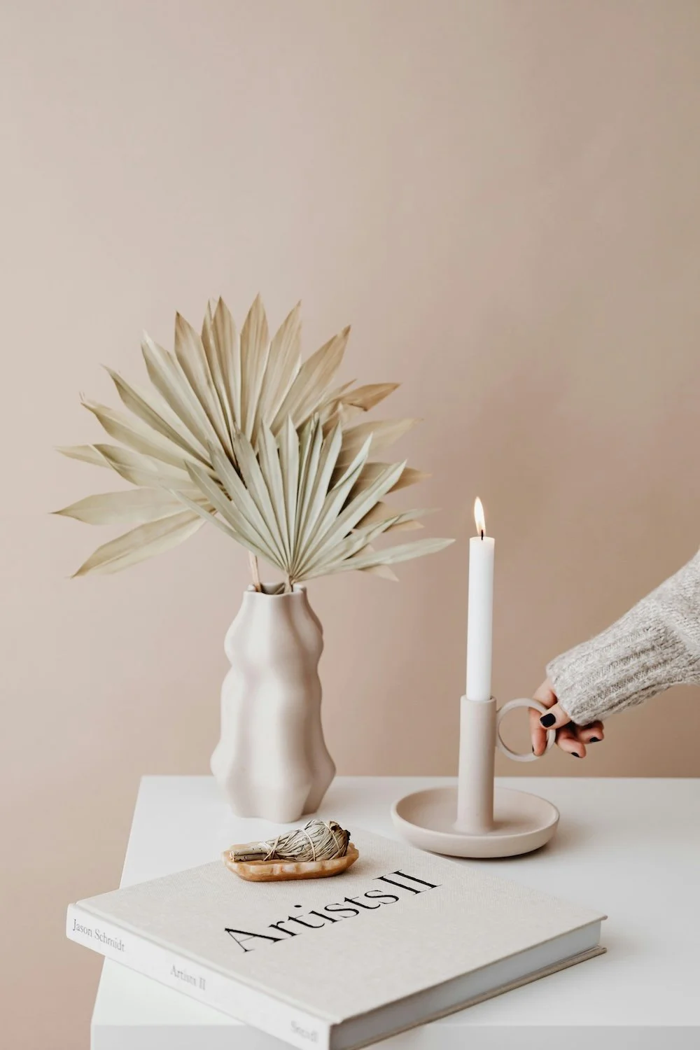 Styled image in neutral tones of a vase, candlestick, book and sage stick 