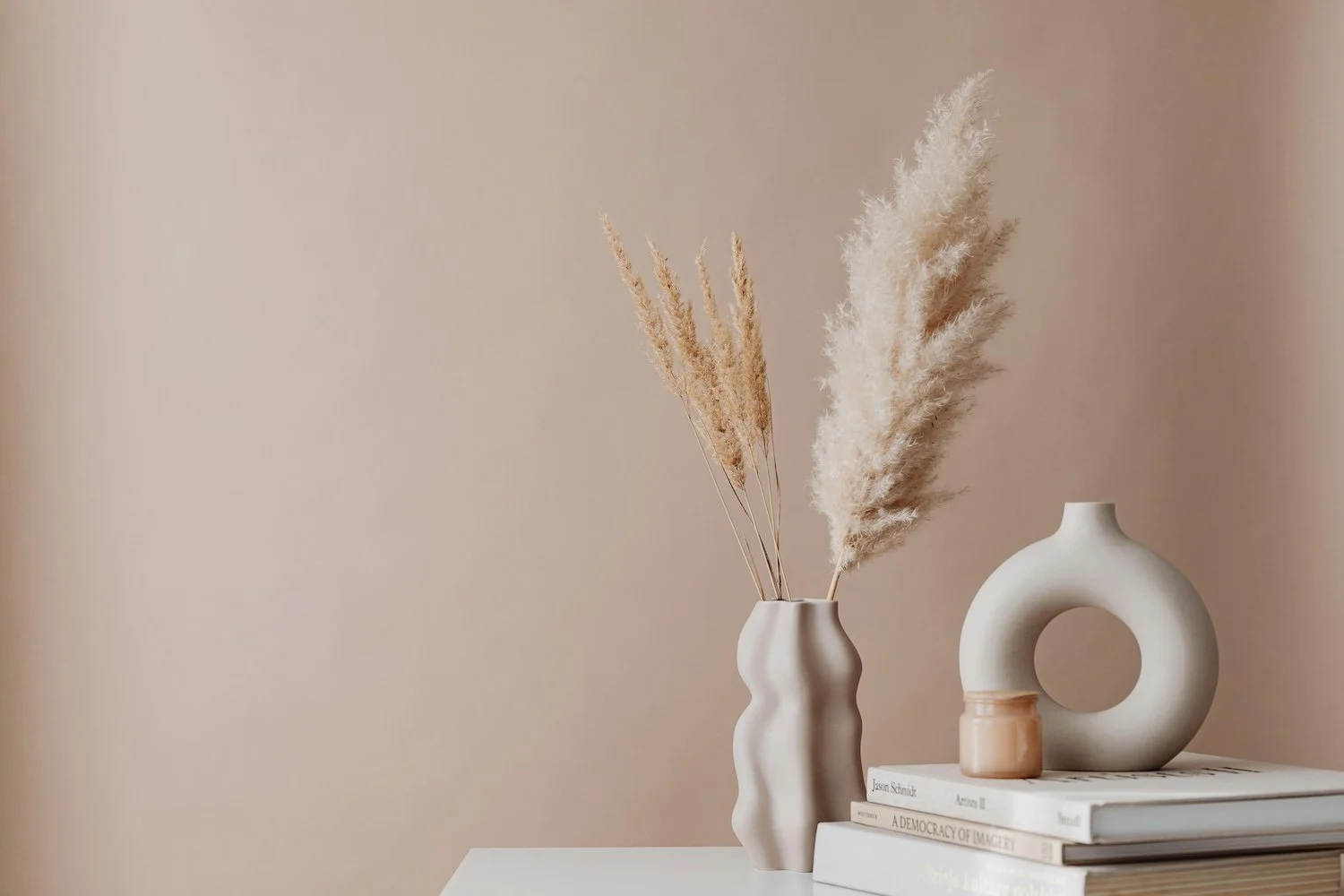 Stylised still life photo of some vases with pampas grass and books in neutral tones