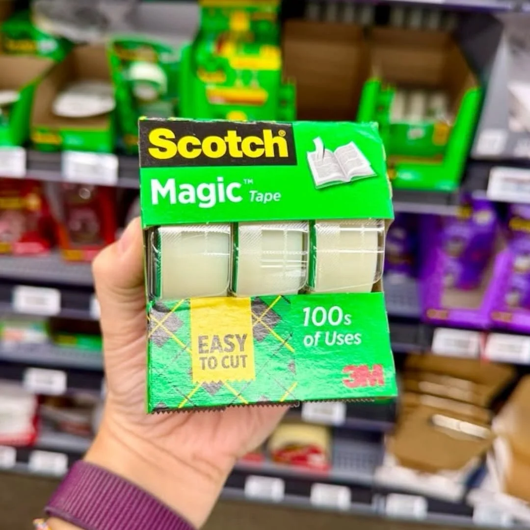 Hand holding a 3-pack of Scotch Magic Tape in green packaging, displayed in a retail store aisle