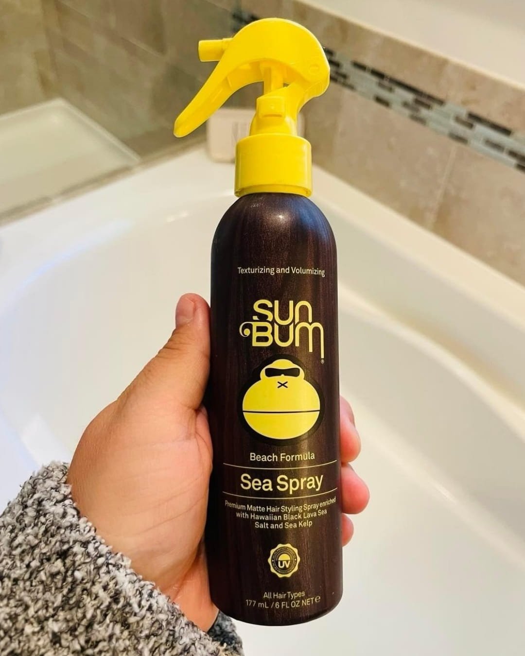 Sun Bum Sea Spray texturizing hair spray bottle with yellow trigger nozzle held in hand