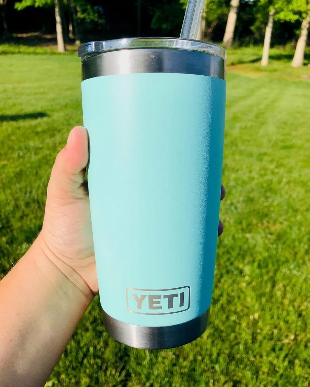 Light blue YETI straw cup with clear lid and straw held outdoors over green grass