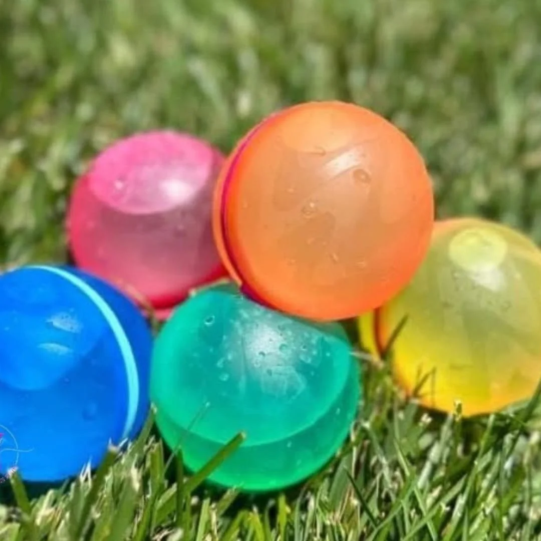 Colorful reusable water balloon balls in orange, green, blue, pink, and yellow resting on grass with water droplets on the surface