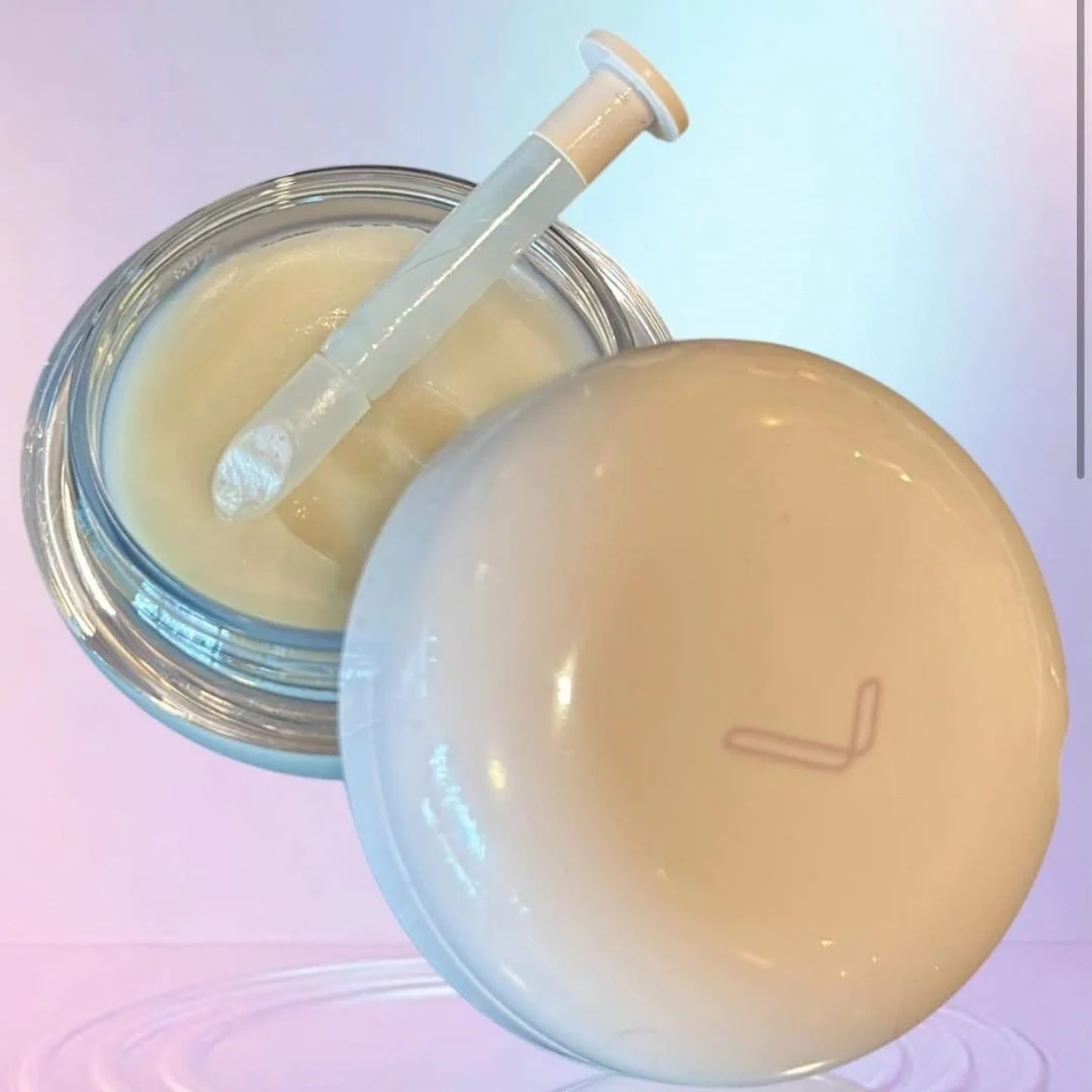 LANEIGE lip care balm in a clear round jar with pale yellow cream, accompanied by a beige applicator and lid, set against a soft blue-to-pink gradient background.