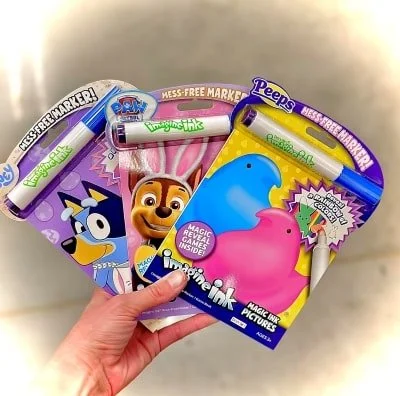 Hand holding three Imagine Ink mess-free coloring sets featuring Bluey, Paw Patrol, and Peeps designs, each with a marker and magic reveal activities for kids.