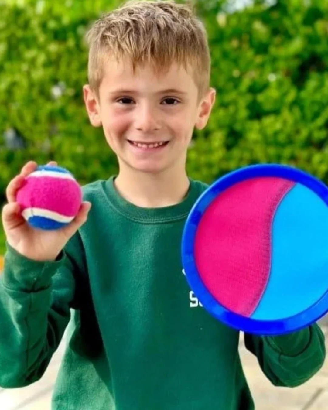 Smiling boy holding colorful ball and paddle outdoors.