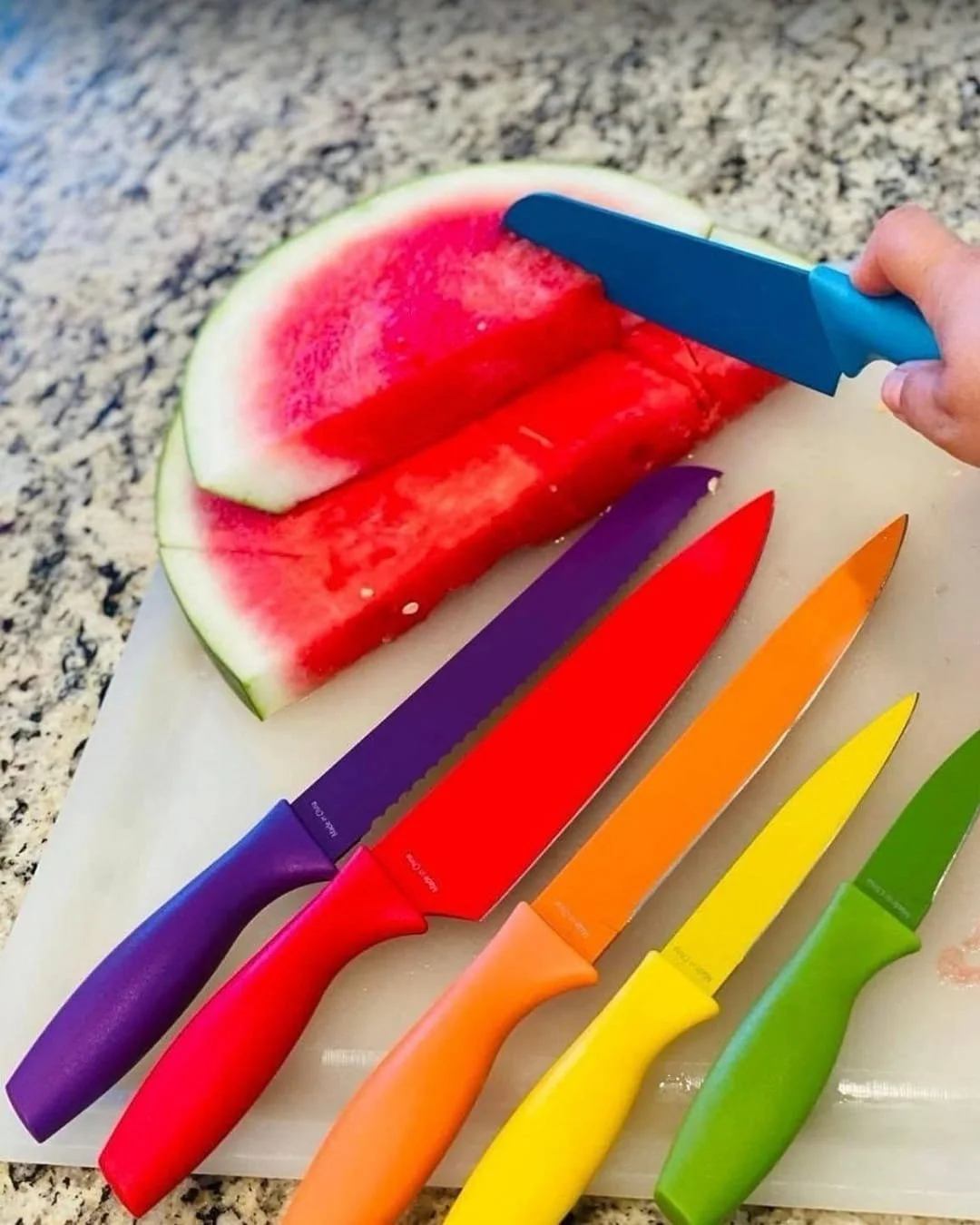 Colorful Amazon kitchen knife set with rainbow-coated blades arranged on a cutting board beside sliced watermelon