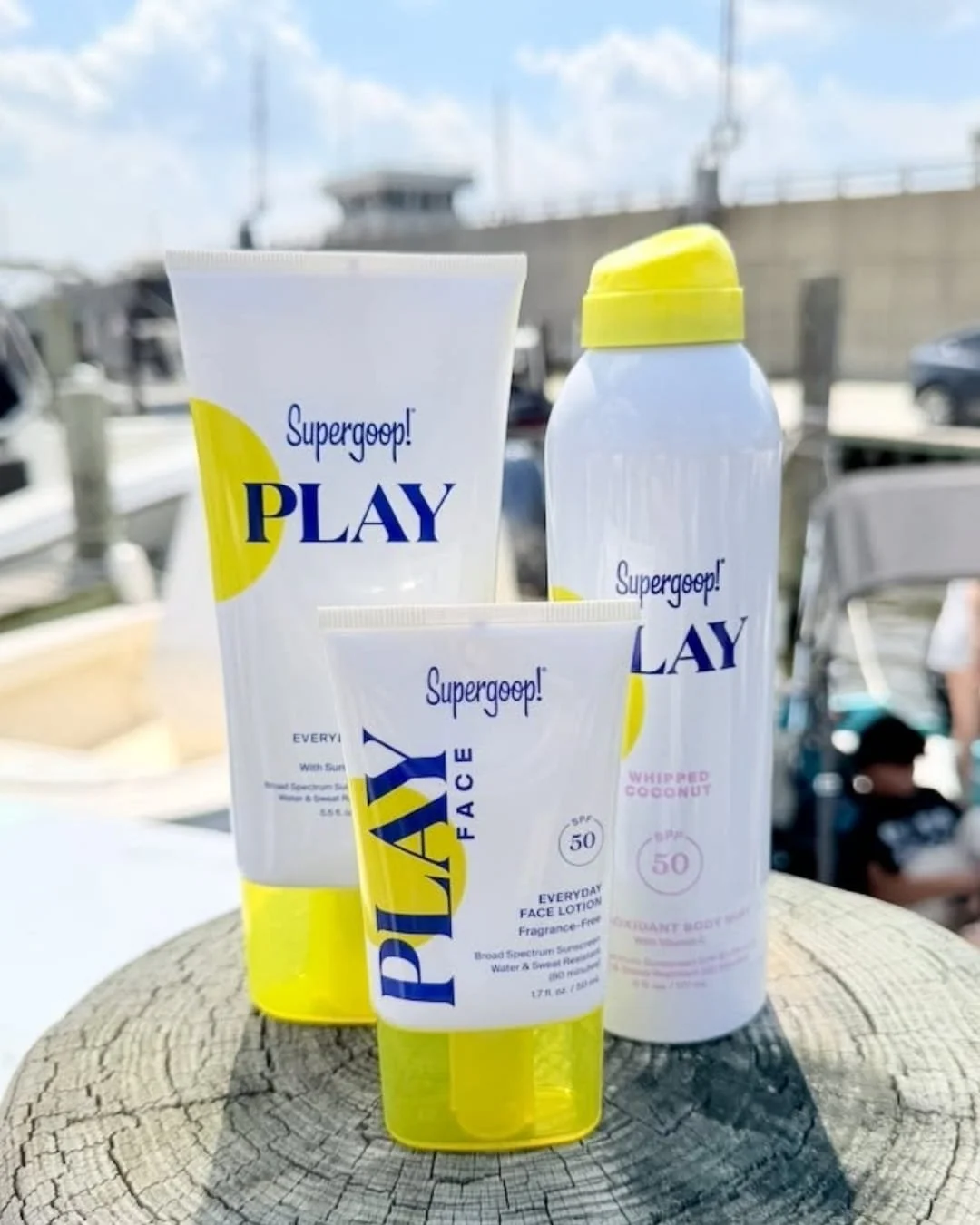 Supergoop Play sunscreen set with body lotion, face lotion, and body mist displayed outdoors near a marina