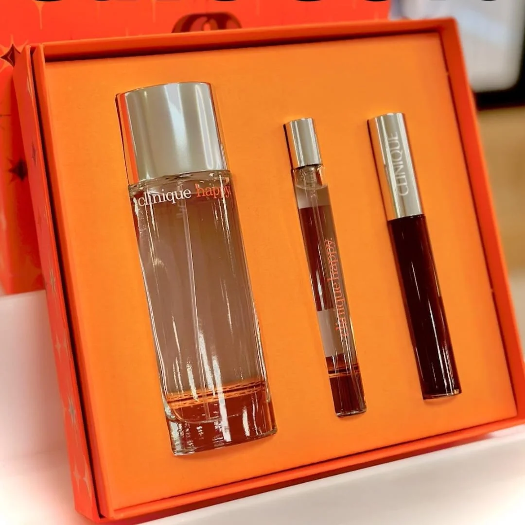 Clinique Happy gift set featuring a large fragrance bottle, travel-size rollerball, and body lotion, presented in a vibrant orange box.