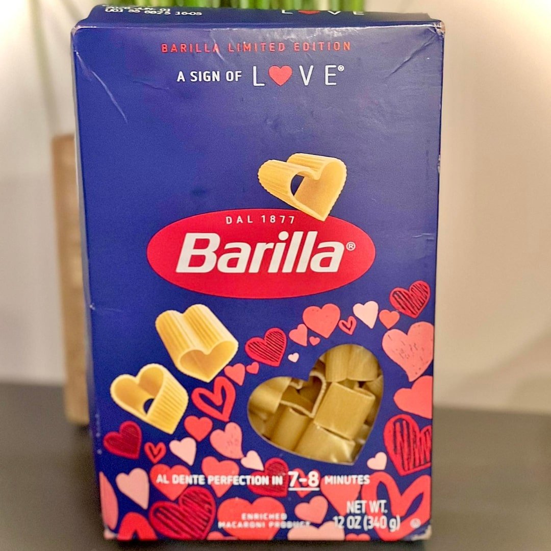 Barilla limited edition heart-shaped pasta box with a love-themed design, featuring a heart-shaped window revealing golden pasta, set against a blurred background.