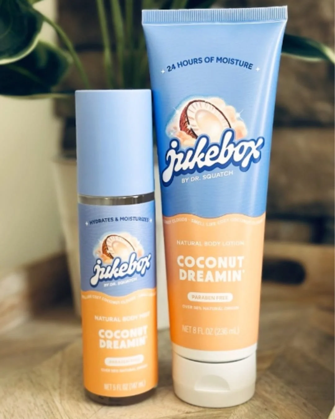 Jukebox by Dr. Squatch Coconut Dreamin’ Body Lotion and Body Mist with tropical blue and orange packaging, featuring coconut graphics, displayed on a wooden surface with blurred green leaves in the background.