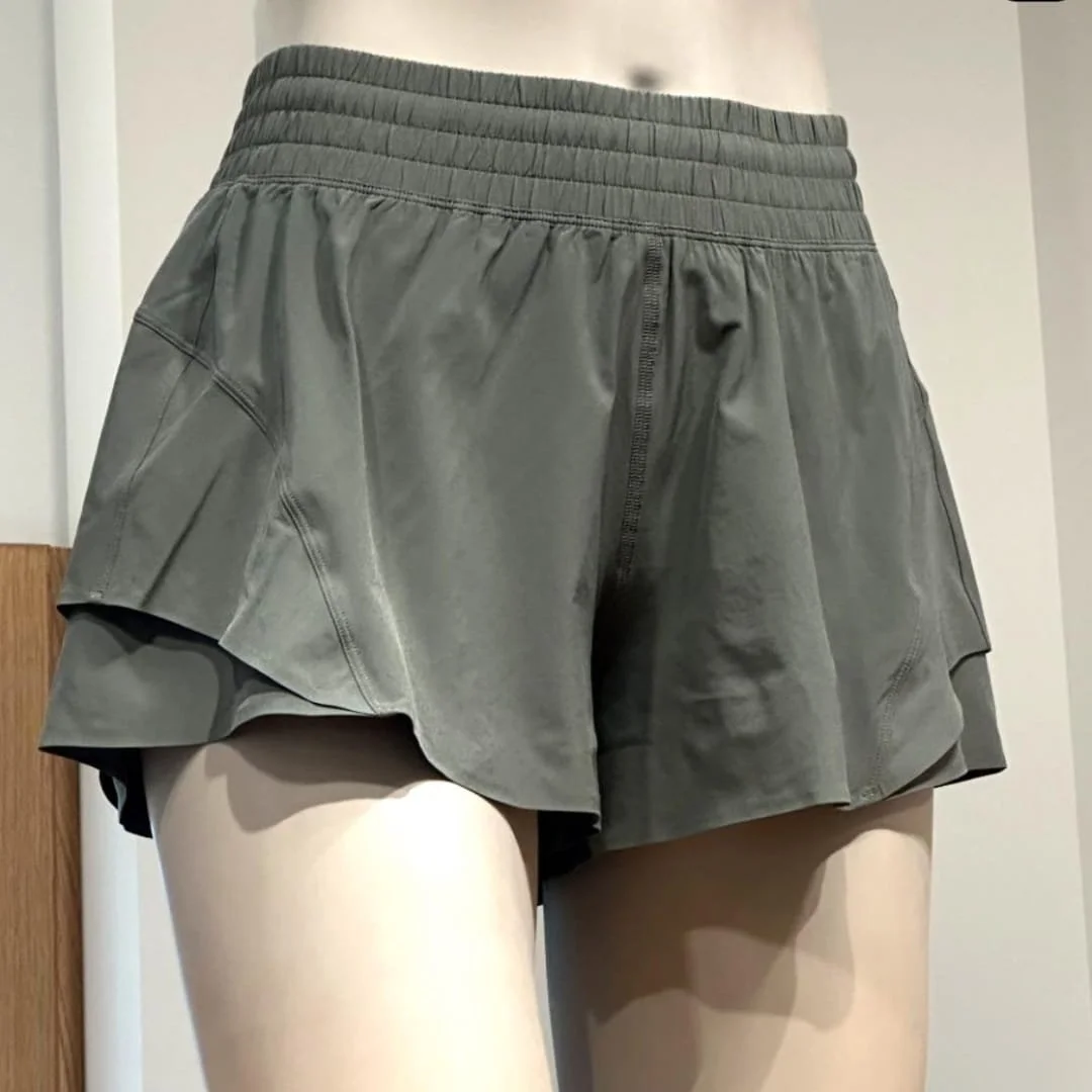 Lululemon dark olive green running shorts with a high-waisted ruched waistband and layered flowy design, displayed on a mannequin in a retail setting.