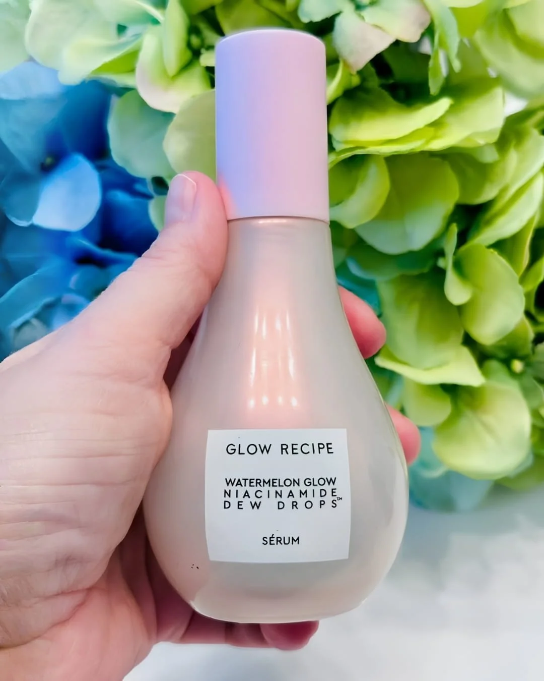 Glow Recipe Watermelon Glow Niacinamide Dew Drops face serum bottle held in hand with floral background