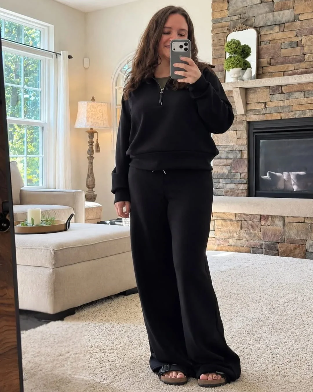 Nicole wearing a black SPANX AirEssentials half-zip top and wide-leg pants in a cozy living room mirror selfie