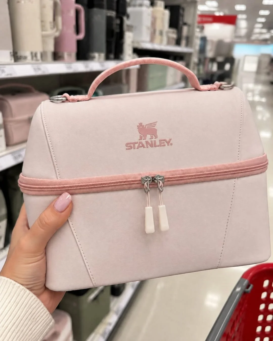 Hand holding a pink STANLEY lunch box with top handle and zipper compartments in a retail store aisle