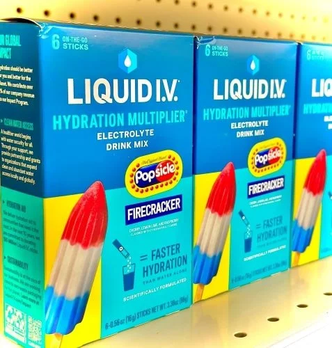 Retail shelf displaying Liquid I.V. Hydration Multiplier boxes in Popsicle Firecracker flavor, featuring red, white, and blue popsicle graphics, highlighting faster hydration benefits and on-the-go stick packs.