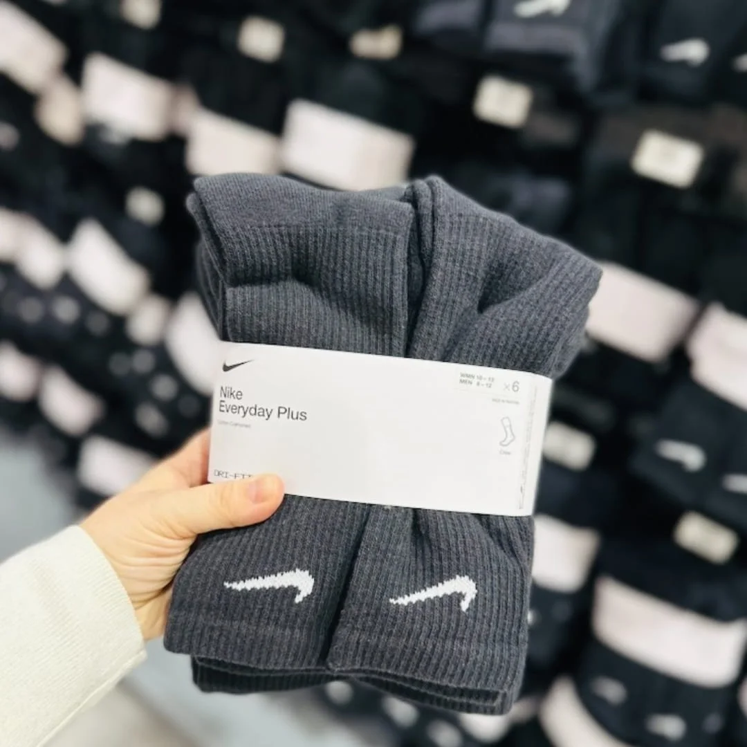 Nike Everyday Plus crew socks in dark gray with white swoosh logo, featuring Dri-Fit and cotton cushioning, bundled in a six-pair pack with sizing for men and women.