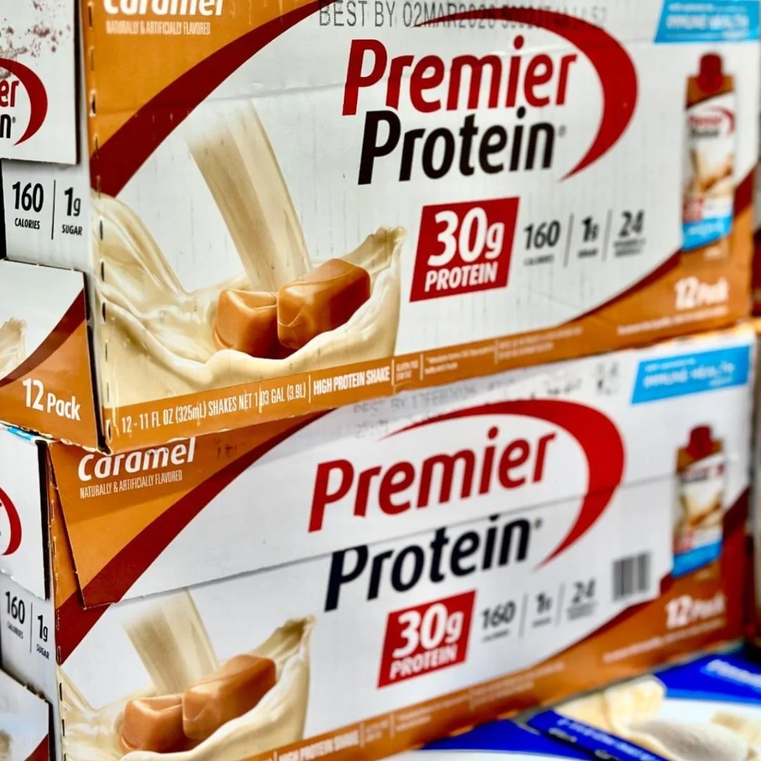 Premier Protein Caramel-flavored high-protein shake 12-pack boxes, featuring 30g protein, 160 calories, and 1g sugar, with vibrant branding and caramel splash imagery.