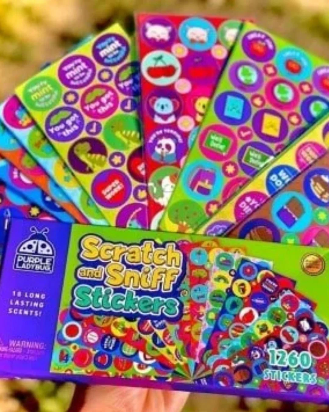 Box of Purple Ladybug Scratch and Sniff Stickers with 1260 colorful stickers and 18 long-lasting scents, displayed with fanned-out sticker sheets featuring playful designs and encouraging messages.
