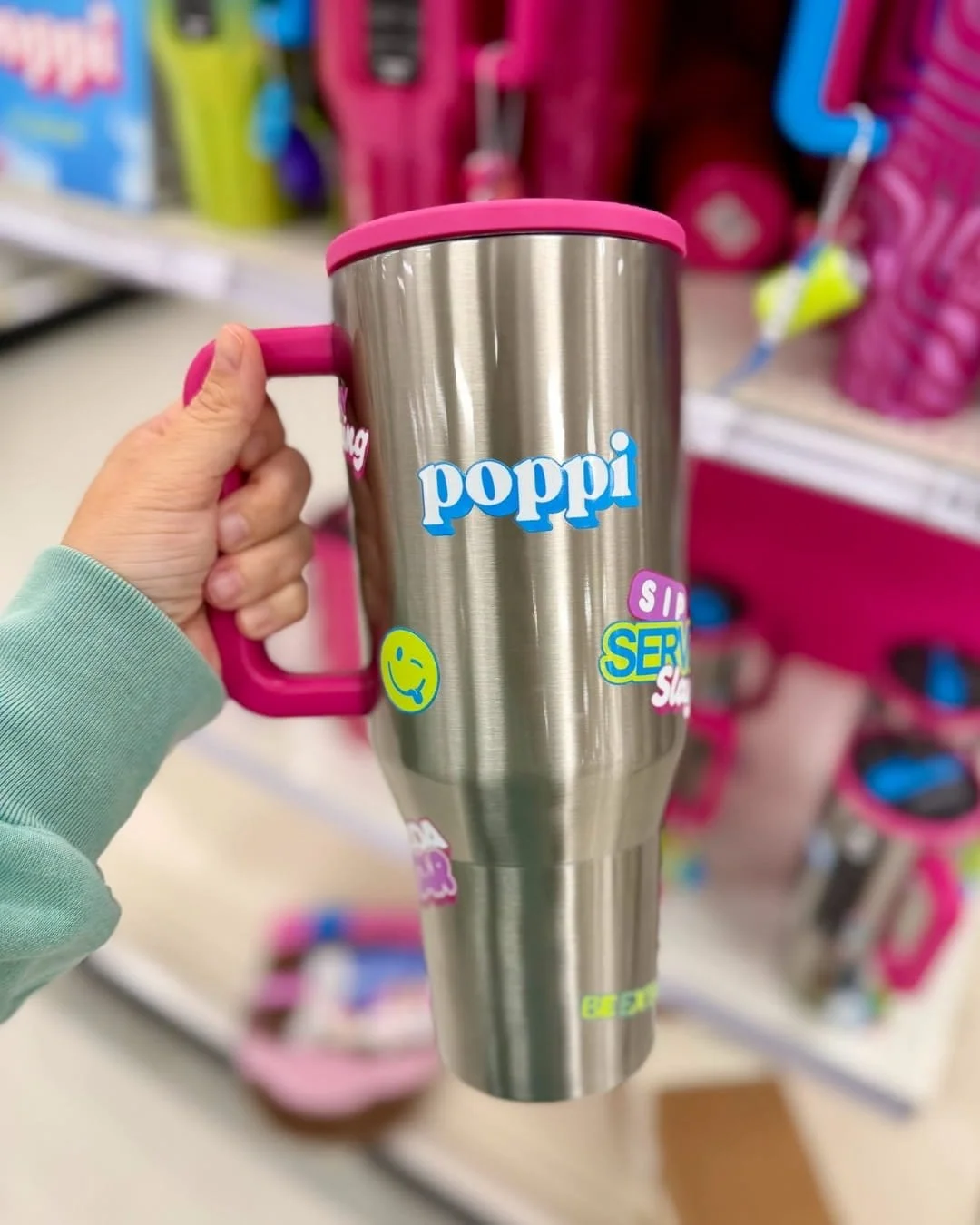 Stainless steel HydroJug tumbler with a pink handle and lid, decorated with colorful stickers, shown in a retail store display