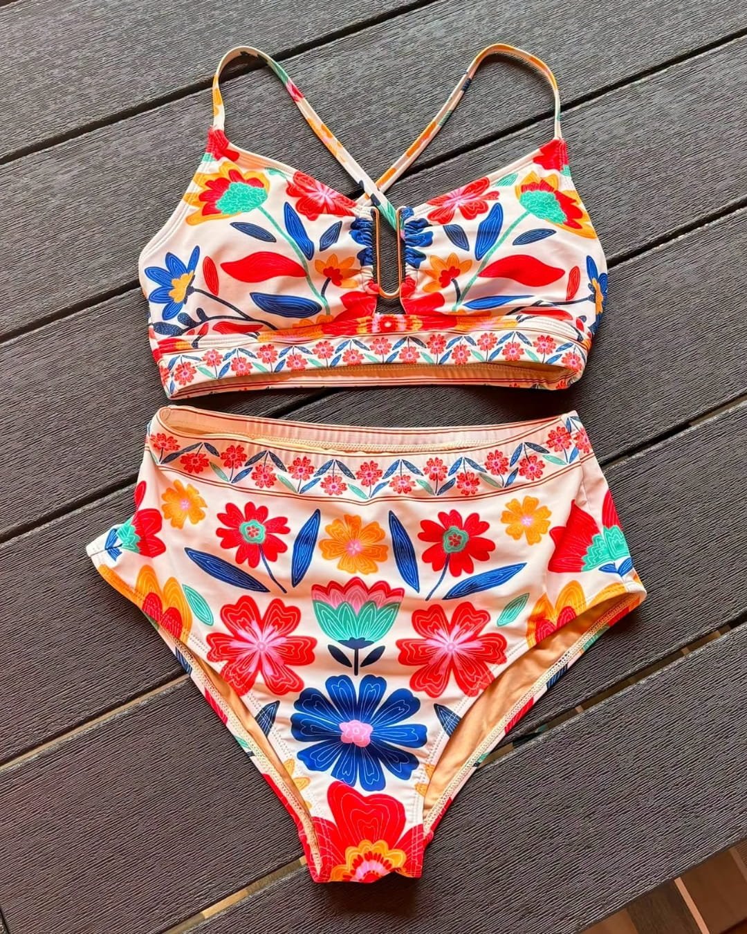 Women’s floral high-waisted bikini set with bralette top and colorful boho print laid flat on wood surface
