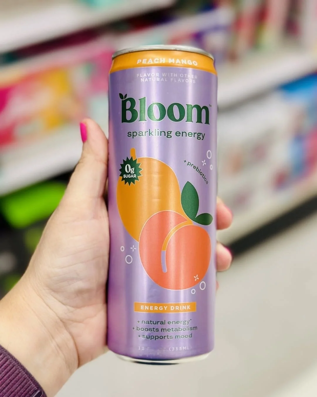 Hand holding a can of Bloom Sparkling Energy Drink Peach Mango flavor in a brightly lit store aisle