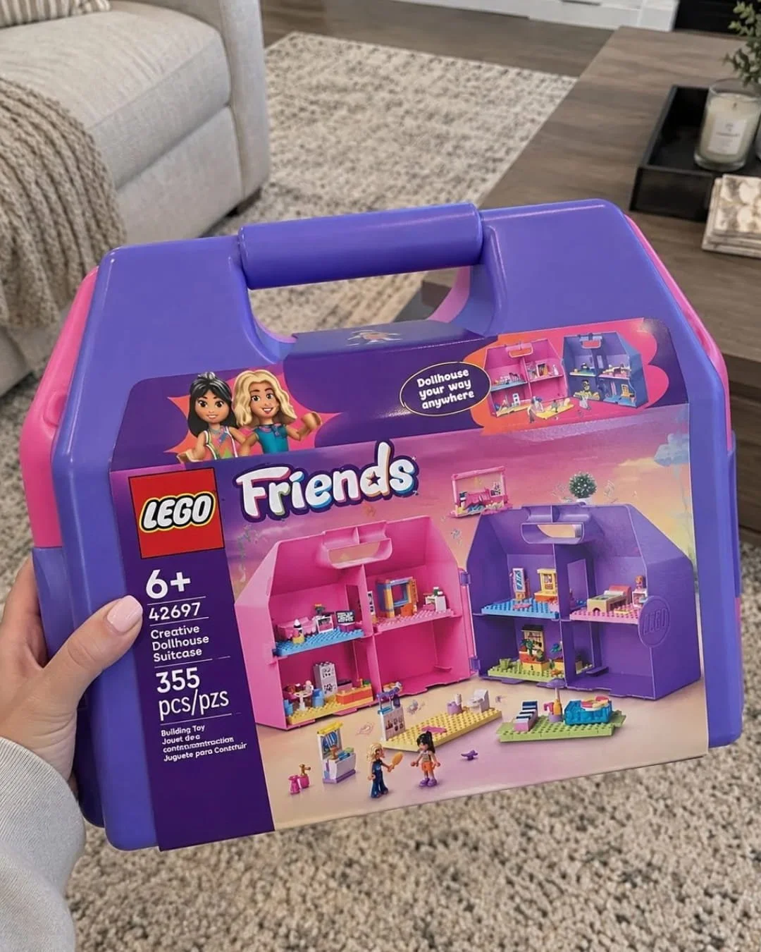 Hand holding LEGO Friends Creative Dollhouse Suitcase building toy with purple carrying case in a living room