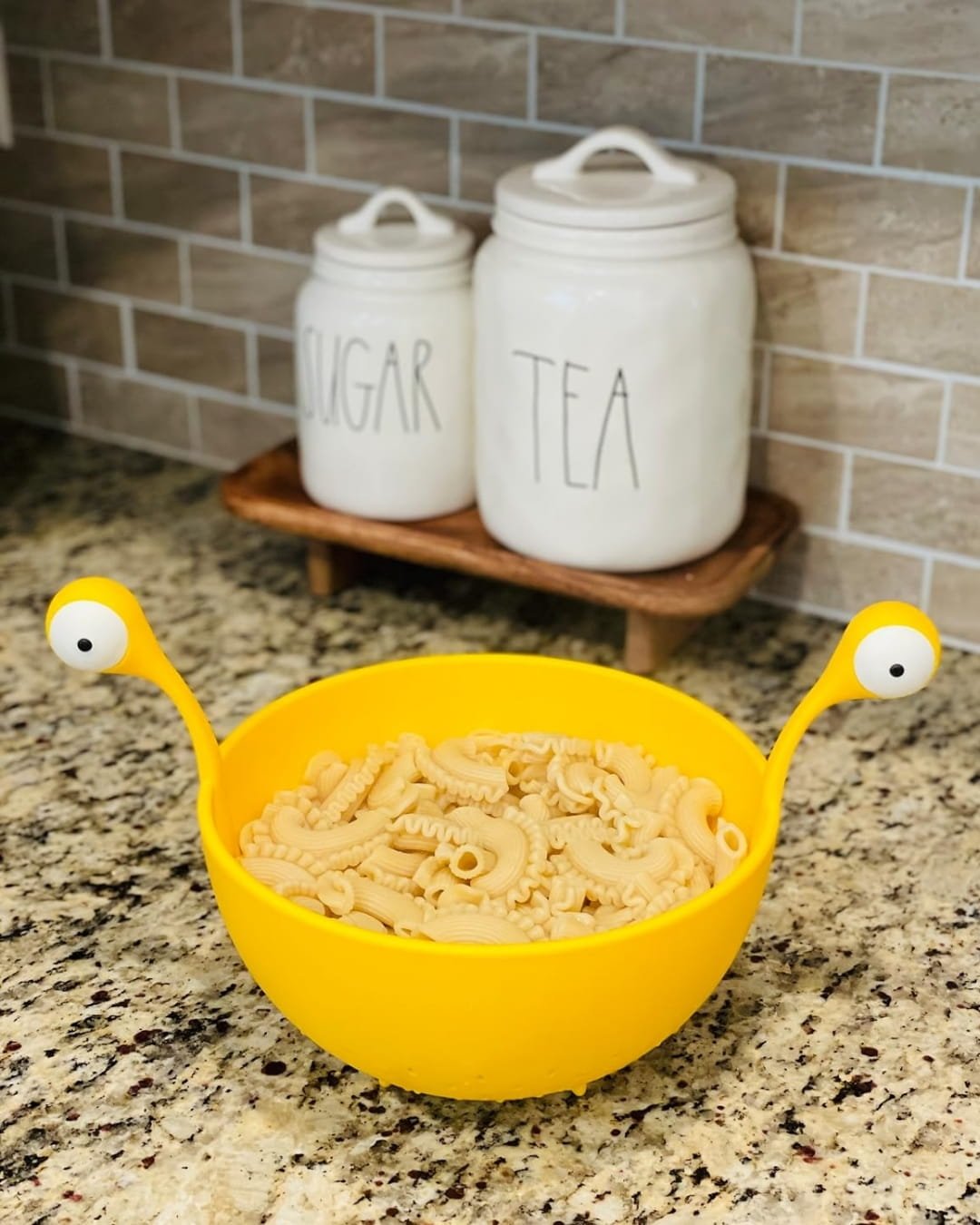 Yellow silicone pasta strainer filled with cooked pasta on a kitchen countertop
